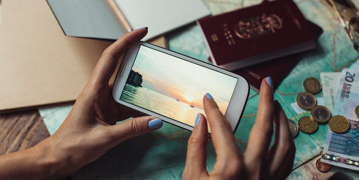 Passport on the table, looking a photo of the ocean and a sailing boats a far on a mobile phone